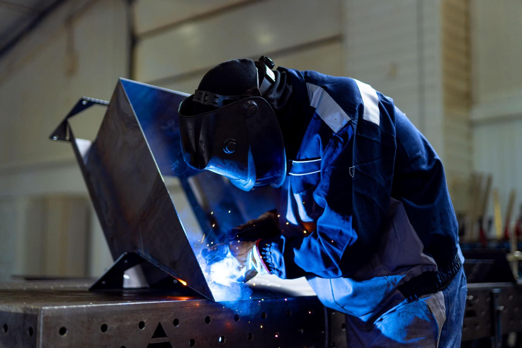 Welder working on a metal enclosure with blue lighting in a fabrication shop