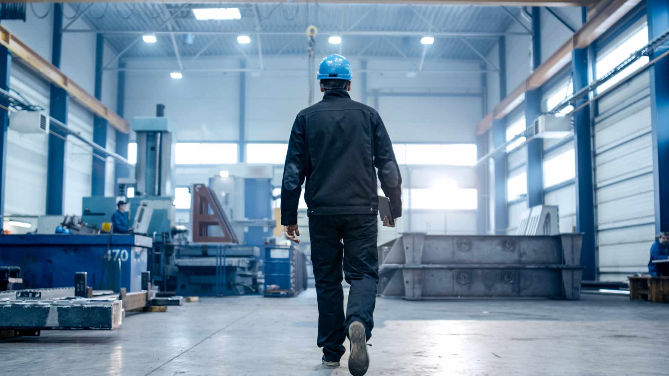 Plant worker in blue hard hat walking through an industrial manufacturing floor