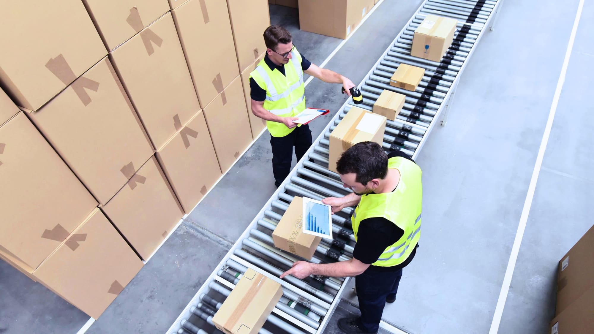 Two warehouse workers scanning and reviewing packages on a conveyor line