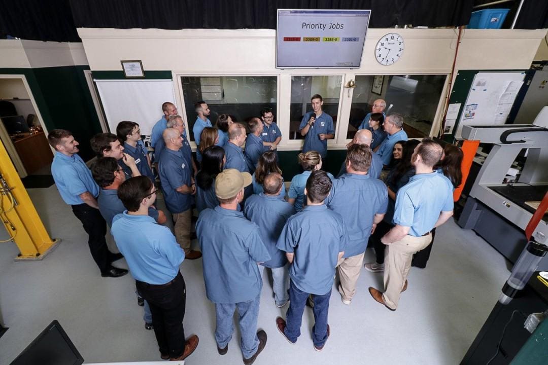 Shop floor team gathered for a morning meeting under a priority jobs board